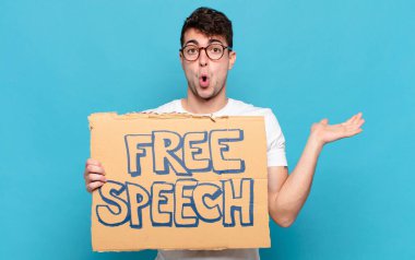 Genç adam şaşırmış ve şok olmuş görünüyor, çenesi düşmüş bir nesneyi elinde açık bir elle tutuyor.