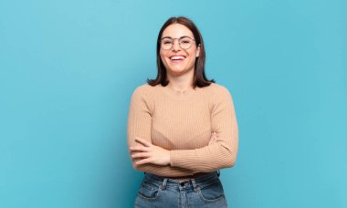 Kollarını kavuşturup gülümseyen mutlu, gururlu ve tatmin olmuş genç ve hoş bir kadın.