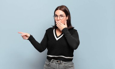 Genç, hoş, sıradan bir kadın kendini mutlu, şok olmuş ve şaşırmış hissediyor. Ağzını eliyle kapatıyor ve yan fotokopi alanını işaret ediyor.