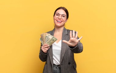 Genç ve güzel bir kadın gülümsüyor ve arkadaş canlısı görünüyor. 5 ya da 5 numarayı gösteriyor.