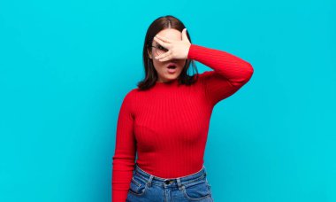 Şok olmuş, korkmuş ya da korkmuş görünen genç, güzel bir kadın. Yüzü elle kaplanmış ve parmaklarının arasından gizlice bakıyor.