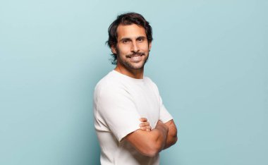 Genç, yakışıklı Hintli adam kameraya çapraz kollarıyla gülümsüyor ve mutlu, kendinden emin, tatmin olmuş bir ifadesi var.