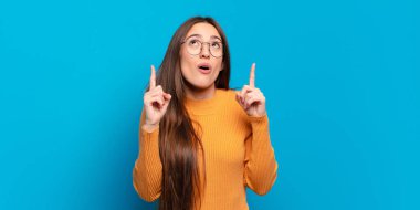 Dehşete kapılmış ve ağzı açık genç bir kadın şaşırmış ve şaşırmış bir bakışla yukarıya bakıyor.