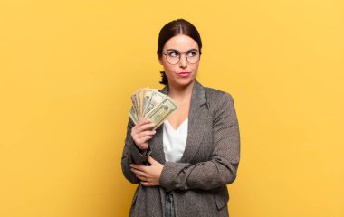 Genç, güzel bir kadın omuz silkiyor, kafası karışık ve kararsız, kolları bağlı ve şaşkın görünüyor.