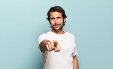 Genç, yakışıklı Hintli adam kameraya bakıyor. Tatmin olmuş, kendine güvenen, dost canlısı bir gülümsemeyle. Seni seçiyor.