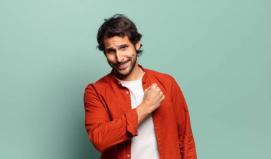 Genç, yakışıklı Hintli bir adam mutlu, pozitif ve başarılı hissediyor, bir meydan okumayla karşılaştığında motive oluyor veya iyi sonuçları kutluyor.