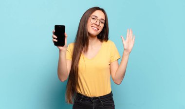 Genç ve güzel bir kadın mutlu ve neşeyle gülümsüyor, el sallıyor, sizi selamlıyor ve selamlıyor, ya da veda ediyor.