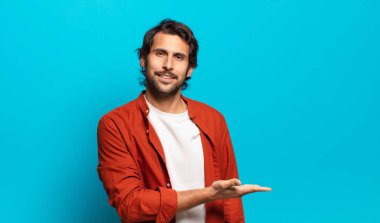 Genç, yakışıklı Hintli adam neşeyle gülümsüyor, mutlu hissediyor ve fotokopi uzayı içinde avucuyla bir konsept gösteriyor.