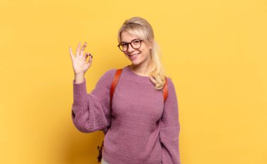 Sarışın kadın kendini mutlu, rahat ve tatmin olmuş hissediyor. Onayını iyi bir hareketle gösteriyor.