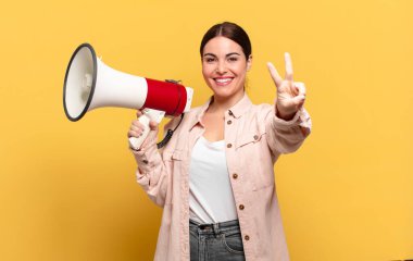 Genç ve güzel bir kadın gülümsüyor ve mutlu görünüyor, kaygısız ve pozitif, zafer ya da barış işareti yapıyor.