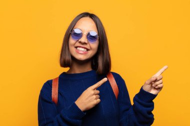 İspanyol kadın mutlu bir şekilde gülümsüyor ve her iki elini de fotokopi alanında objeler gösteriyor.