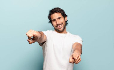 Genç ve yakışıklı Hintli adam mutlu ve kendinden emin, kamerayı iki eliyle gösteriyor ve gülüyor, seni seçiyor.