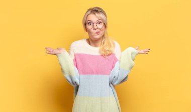 Sarışın kadın şaşkın ve şaşkın hissediyor, şüpheci, farklı seçenekleri tartıyor veya komik bir ifadeyle seçiyor.