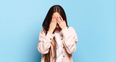 Genç, hoş, sıradan bir kadın üzgün, hayal kırıklığına uğramış, gergin ve depresif, iki eliyle yüzünü kaplayan, ağlayan.