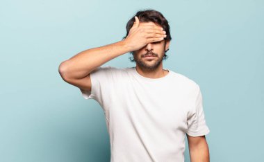 Genç ve yakışıklı Hintli bir adam tek eliyle gözlerini kapatıyor korkmuş ya da endişeli hissediyor, merak ediyor ya da körü körüne bir sürpriz bekliyor.