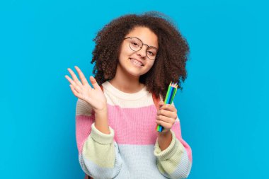 Güzel afro genç mutlu ve neşeyle gülümsüyor, el sallıyor, sizi selamlıyor ve selamlıyor, ya da veda ediyor. öğrenci konsepti