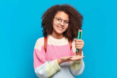 Güzel afro ergen neşeli gülümsüyor, mutlu hissediyor ve fotokopi uzayı içinde avucunun içi gibi bir konsept gösteriyor. öğrenci konsepti