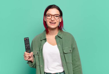 Genç ve çekici kızıl saçlı kadın mutlu ve hoş bir şekilde şaşırmış görünüyor. Büyülenmiş ve şok olmuş bir ifadeyle heyecanlı ve elinde uzaktan kumandayla televizyon izliyor.