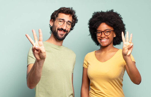 multiracial couple of friends smiling and looking friendly, showing number three or third with hand forward, counting down