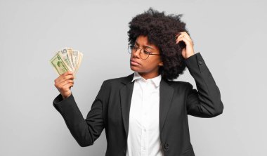 Genç afro iş kadını şaşkın ve şaşkın hissediyor, başını kaşıyor ve yana bakıyor. iş kavramı