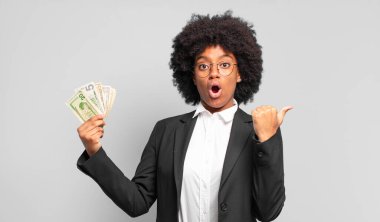 Genç afro iş kadını inançsızlıktan şaşkın şaşkın bakıyor, yan taraftaki objeyi işaret ediyor ve 