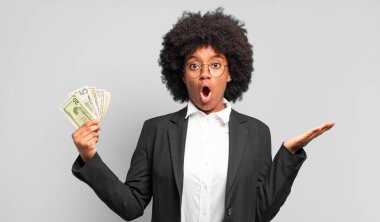 Genç afro iş kadını şaşırmış ve şok olmuş görünüyor. Çenesi düşmüş ve eli açık bir objeyi tutuyor. iş kavramı