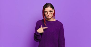  Gururlu, kendinden emin ve mutlu görünüyor, gülümsüyor ve kendini işaret ediyor ya da bir numara işareti yapıyor.