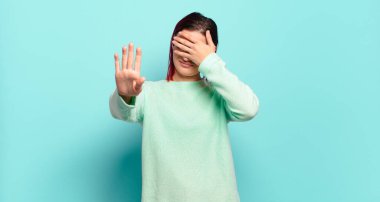  Yüzünü eliyle kapatıyor ve kamerayı durdurmak için diğer elini öne koyuyor, fotoğraf ya da resimleri reddediyor.