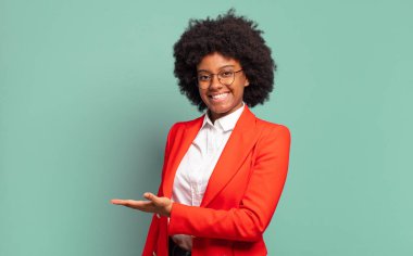  Neşeli bir şekilde gülümsüyor, mutlu hissediyor ve bir konsepti fotokopi uzayında avuç içiyle gösteriyor.