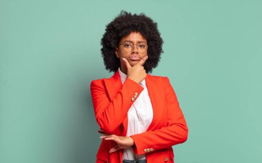  Ciddi görünüyor, düşünceli ve güvensiz, bir kolu çaprazlanmış ve eli çenesinde, seçenekleri değerlendiriyor.