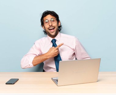 young handsome indian man looking excited and surprised pointing to the side and upwards to copy space. business and frelancer concept