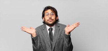 Genç yakışıklı Hintli adam şaşkın ve şaşkın hissediyor, şüpheci, farklı seçenekleri tartıyor ya da komik bir ifadeyle seçiyor. iş kavramı