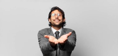 Genç, yakışıklı Hintli adam mutlu bir şekilde gülümsüyor, kendine güvenen, pozitif bakışlı, bir nesne ya da konsept sunuyor ve gösteriyor. iş kavramı