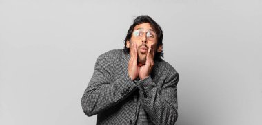 Genç ve yakışıklı Hintli adam şok olmuş ve korkmuş hissediyor, ağzı açık ve elleri yanaklarında korkmuş görünüyor. iş kavramı