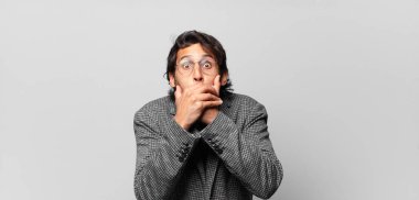 Genç, yakışıklı Hintli bir adam elleri ile ağzını kapatıyor, şok olmuş, şaşırmış bir ifadeyle, sır saklıyor ya da 