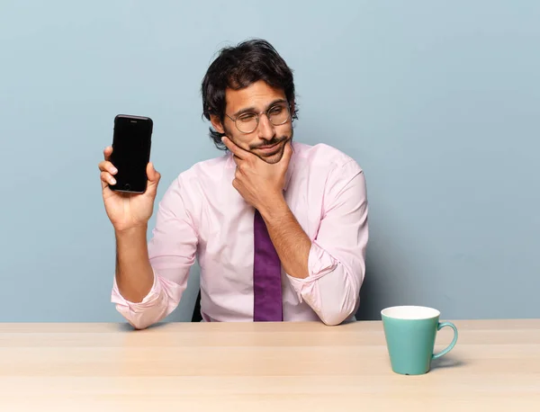 young handsome indian man smiling with a happy, confident expression with hand on chin, wondering and looking to the side. business concept