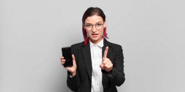 Genç ve çekici kızıl saçlı kadın gururla gülümsüyor ve bir numaralı pozunu başarıyla veriyor, kendini lider gibi hissediyor. iş kavramı