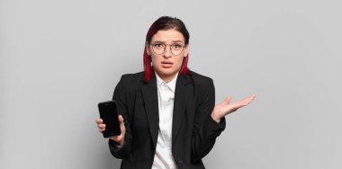 Genç ve çekici kızıl saçlı kadın şaşırmış ve şok olmuş görünüyor. Çenesi düşmüş ve eli açık bir objeyi tutuyor. iş kavramı