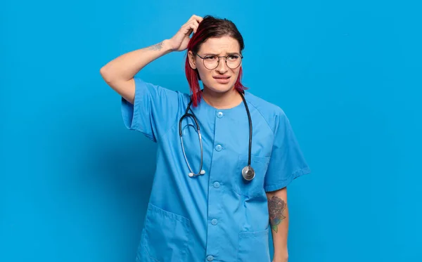 若い魅力的な赤い髪の女性は困惑し 混乱し 頭を引っ掻き 側面を探しています 病院看護師のコンセプト — ストック写真