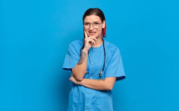 若い魅力的な赤い髪の女性は幸せそうな表情で笑っている顎を手に 疑問に思って横を見ている 病院看護師のコンセプト — ストック写真