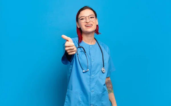 年轻迷人的红头发女人感到自豪 无忧无虑 自信和快乐 微笑着竖起大拇指 医院护士概念 — 图库照片