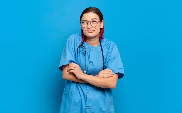 若い魅力的な赤い髪の女性の肩をすくめ 混乱し 不確定な感じ 腕を疑い 困惑している表情 病院看護師のコンセプト — ストック写真
