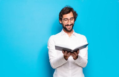 Mavi arkaplan üzerine kitabı olan genç sakallı adam.