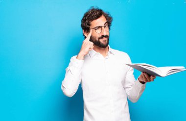 Mavi arkaplan üzerine kitabı olan genç sakallı adam.