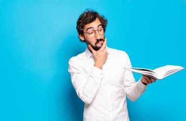 Mavi arkaplan üzerine kitabı olan genç sakallı adam.