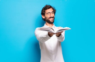 Mavi arkaplan üzerine kitabı olan genç sakallı adam.