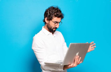 Genç sakallı adam dizüstü bilgisayar tutuyor.