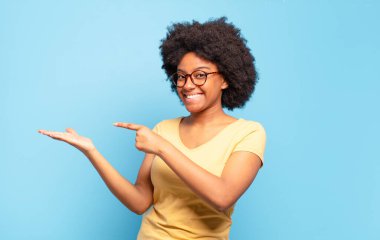  Gülümsüyor ve bir objeyi göstererek veya reklamını yaparak avucunun içindeki kopyalama alanını işaret ediyor.