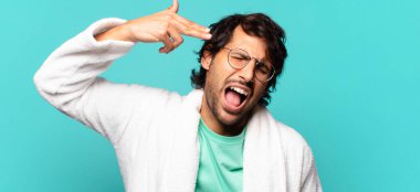 Genç ve yakışıklı Hintli adam mutsuz ve stresli görünüyor, intihar jesti elle silah işareti yapıyor, kafasını işaret ediyor ve banyo cübbesi giyiyor.