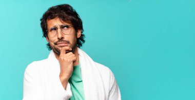 Genç, yakışıklı Hintli adam düşünüyor, kuşkulu ve şaşkın hissediyor, farklı seçenekleri var, hangi kararı vereceğini merak ediyor ve bornoz giyiyor.